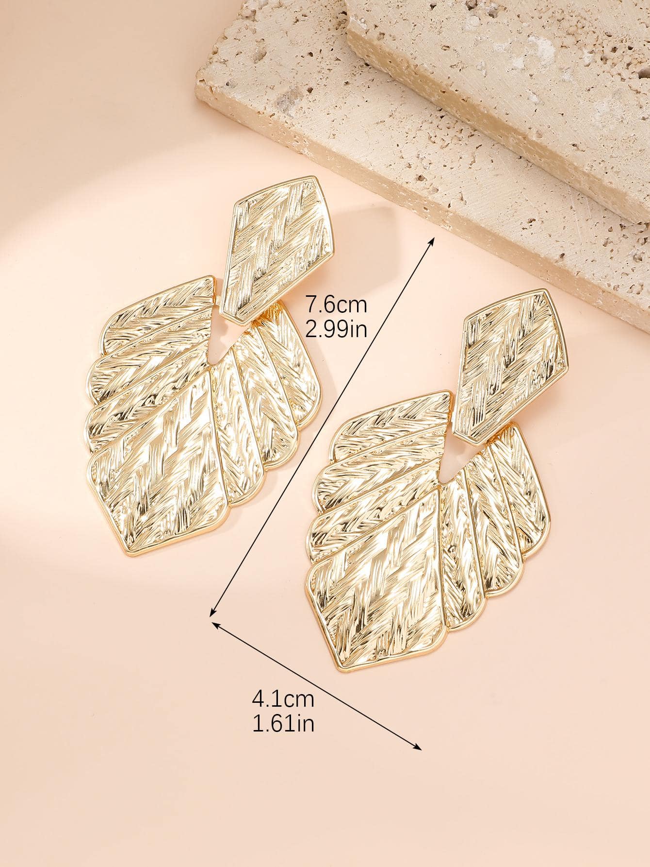Gold leaf-shaped earrings with measurements on a beige background