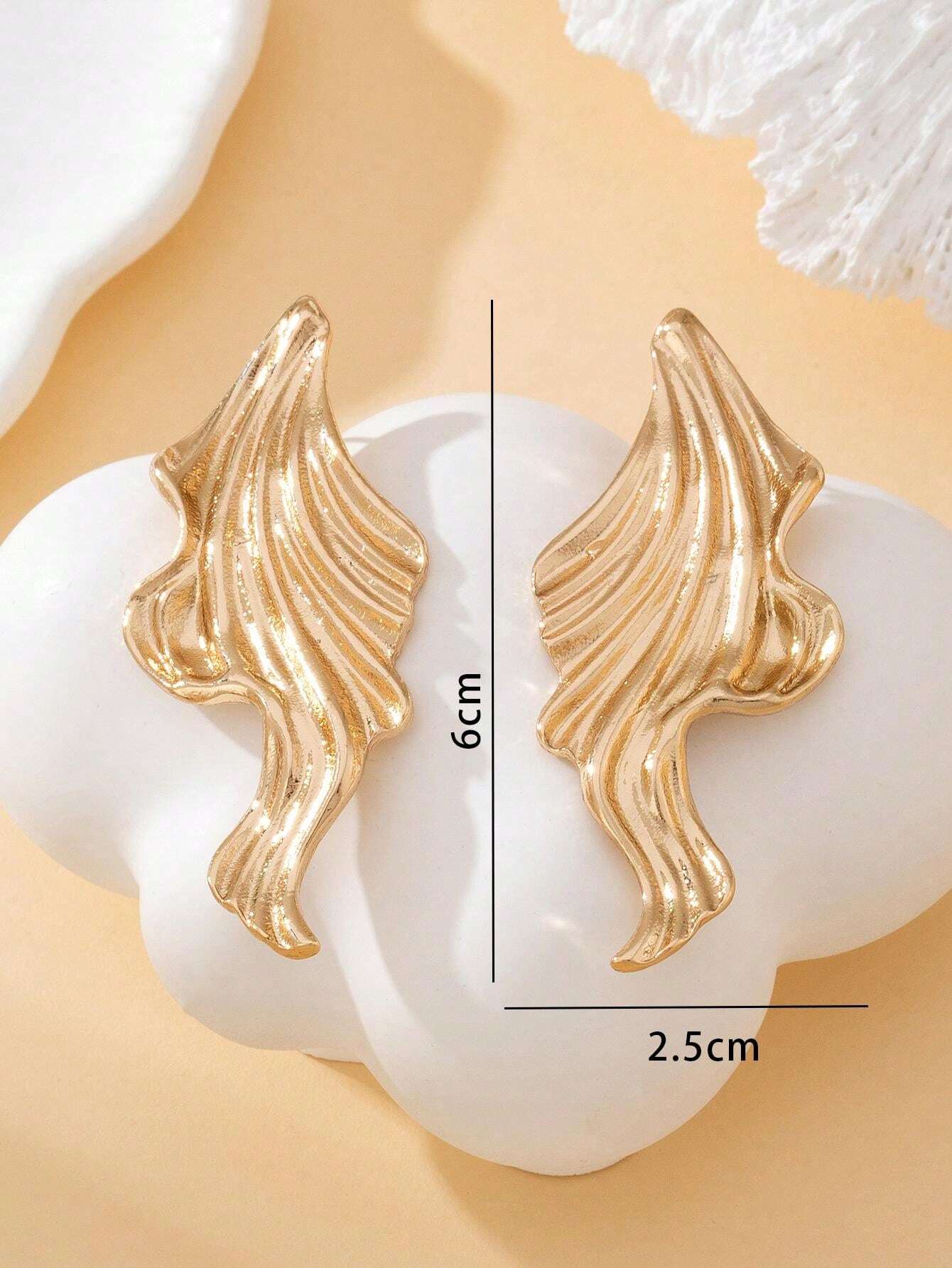 Gold wing-shaped earrings on a white shell with measurements indicated.