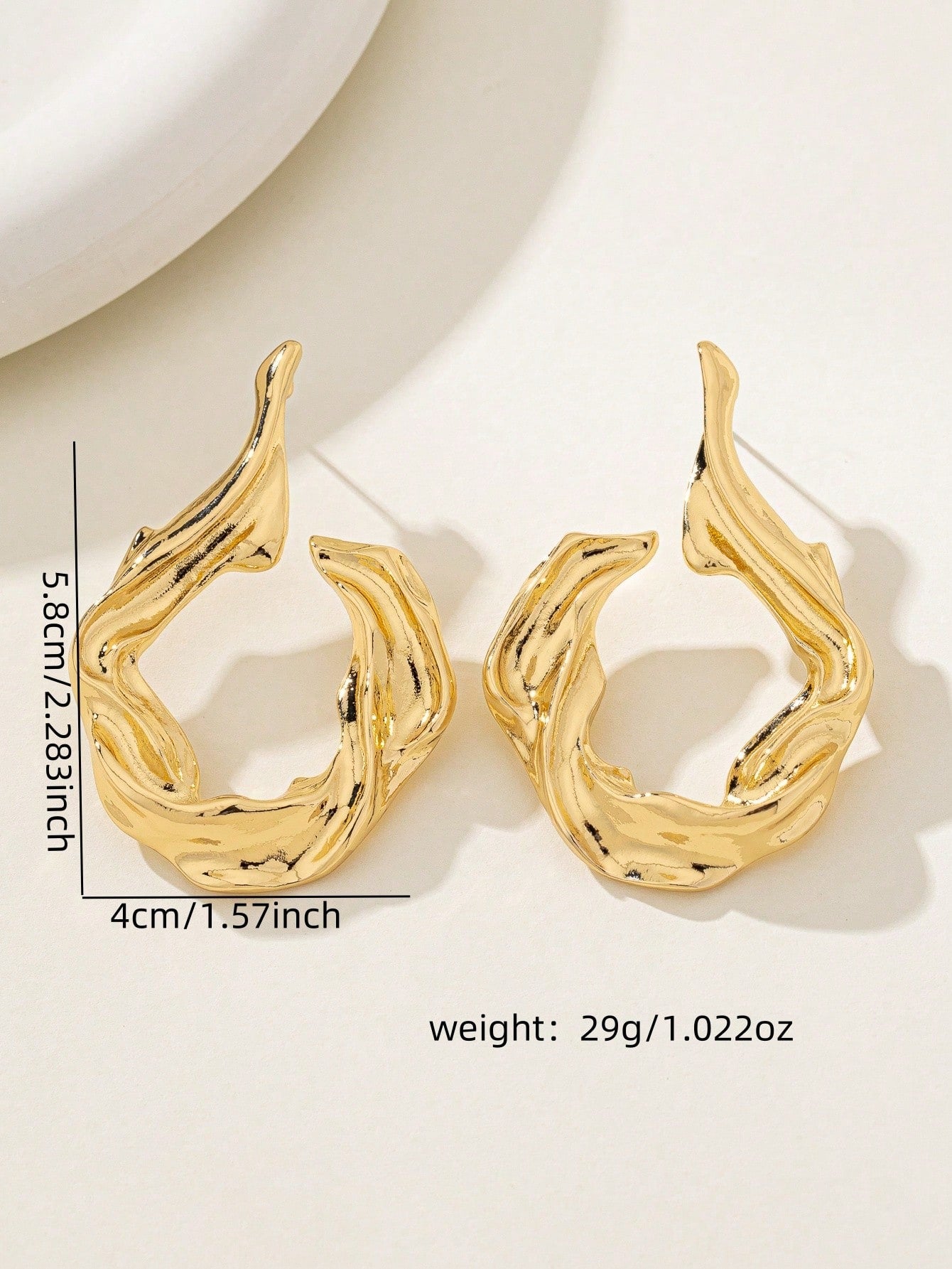 Gold earrings with measurements and weight on a light background