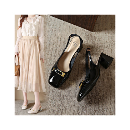 Black patent leather shoes with gold buckles on a textured surface, next to a person wearing a white blouse and beige skirt.
