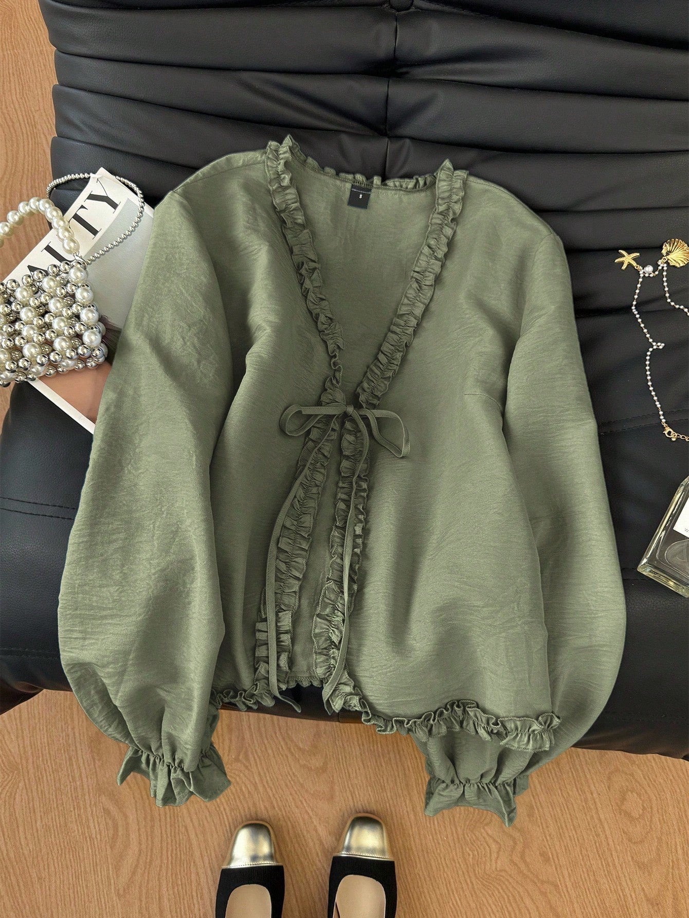 Green frill trim tie-front long-sleeve blouse with delicate ruffles laid flat on a dark textured background