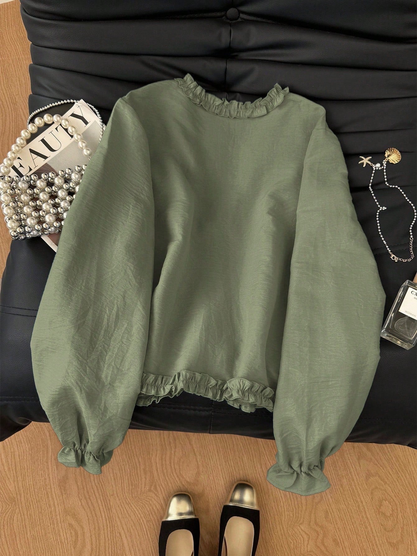 Green frill trim tie-front long-sleeve blouse with delicate ruffles laid flat on a dark textured background