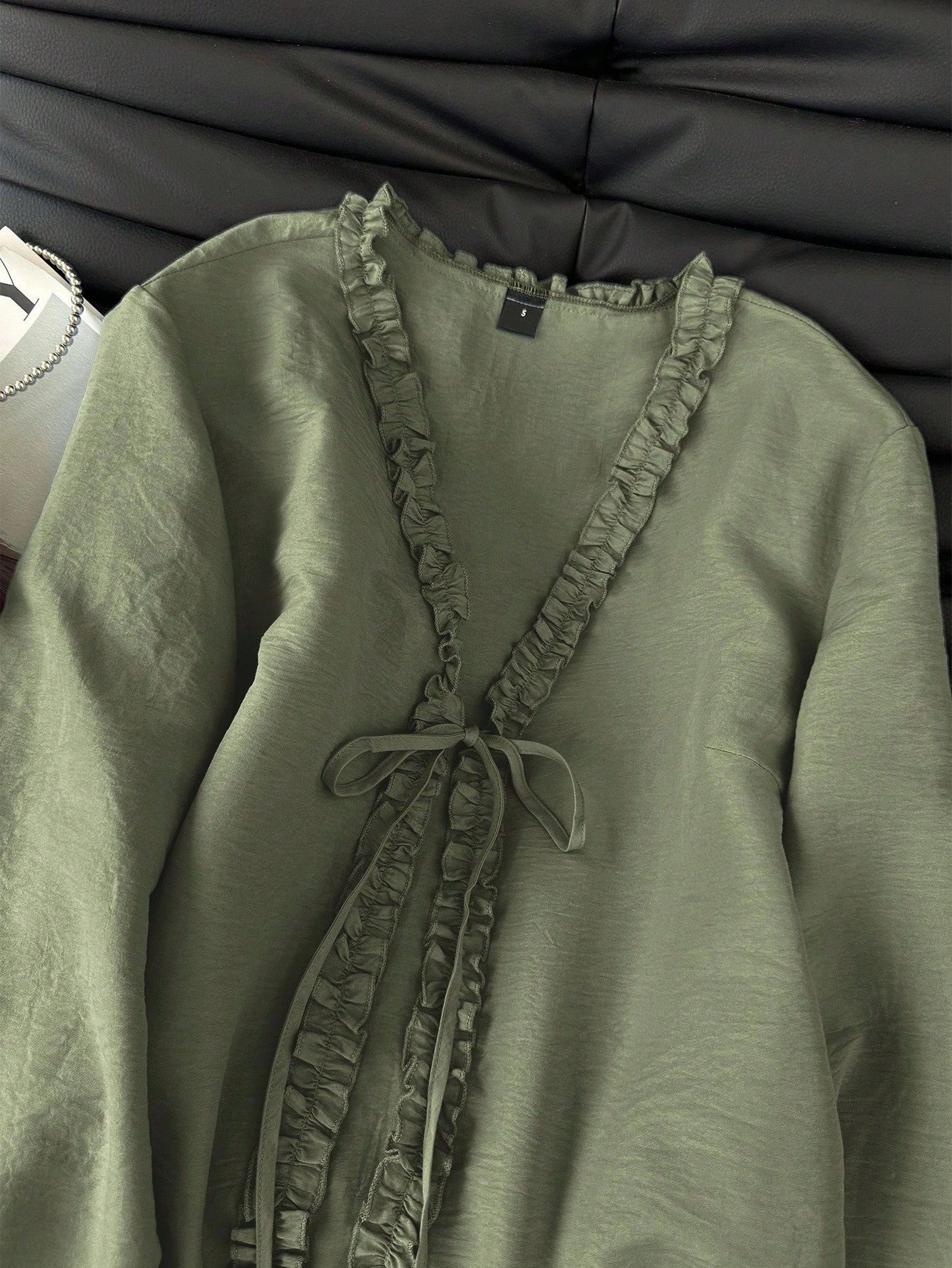 Green frill trim tie-front long-sleeve blouse with delicate ruffles laid flat on a dark textured background