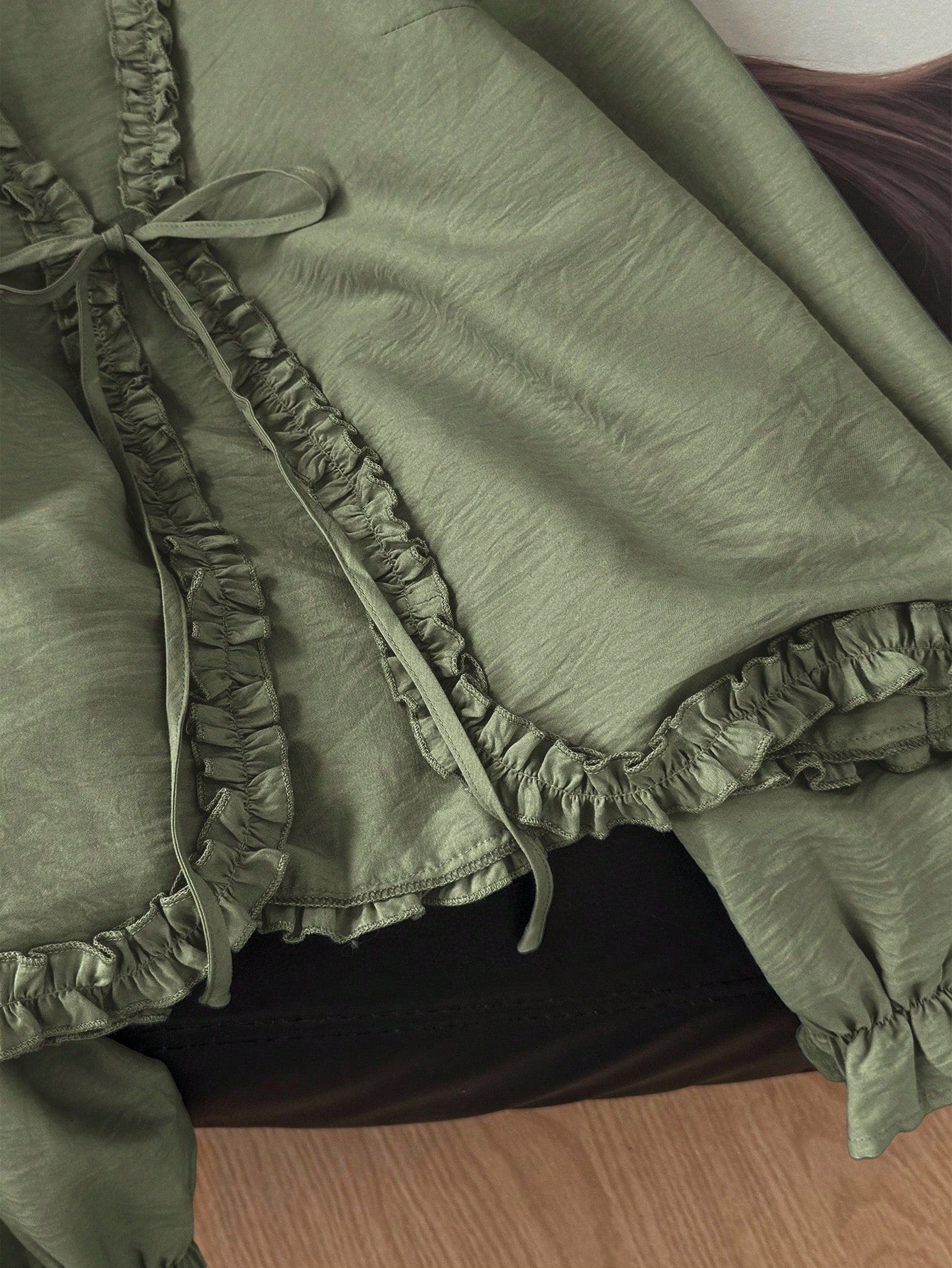 Green frill trim tie-front long-sleeve blouse with delicate ruffles laid flat on a dark textured background