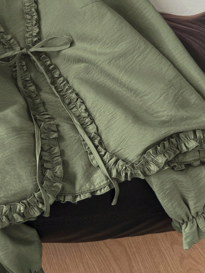 Green frill trim tie-front long-sleeve blouse with delicate ruffles laid flat on a dark textured background