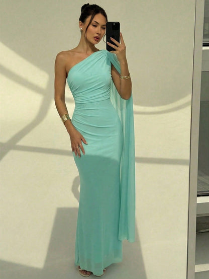A woman wearing an elegant Mint Dress one-shoulder ruched mermaid long dress with a dramatic flutter cloak sleeve