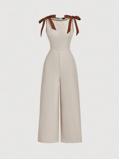Khaki wide-leg sleeveless jumpsuit featuring contrast brown shoulder bow ties and trim laid flat against a neutral background