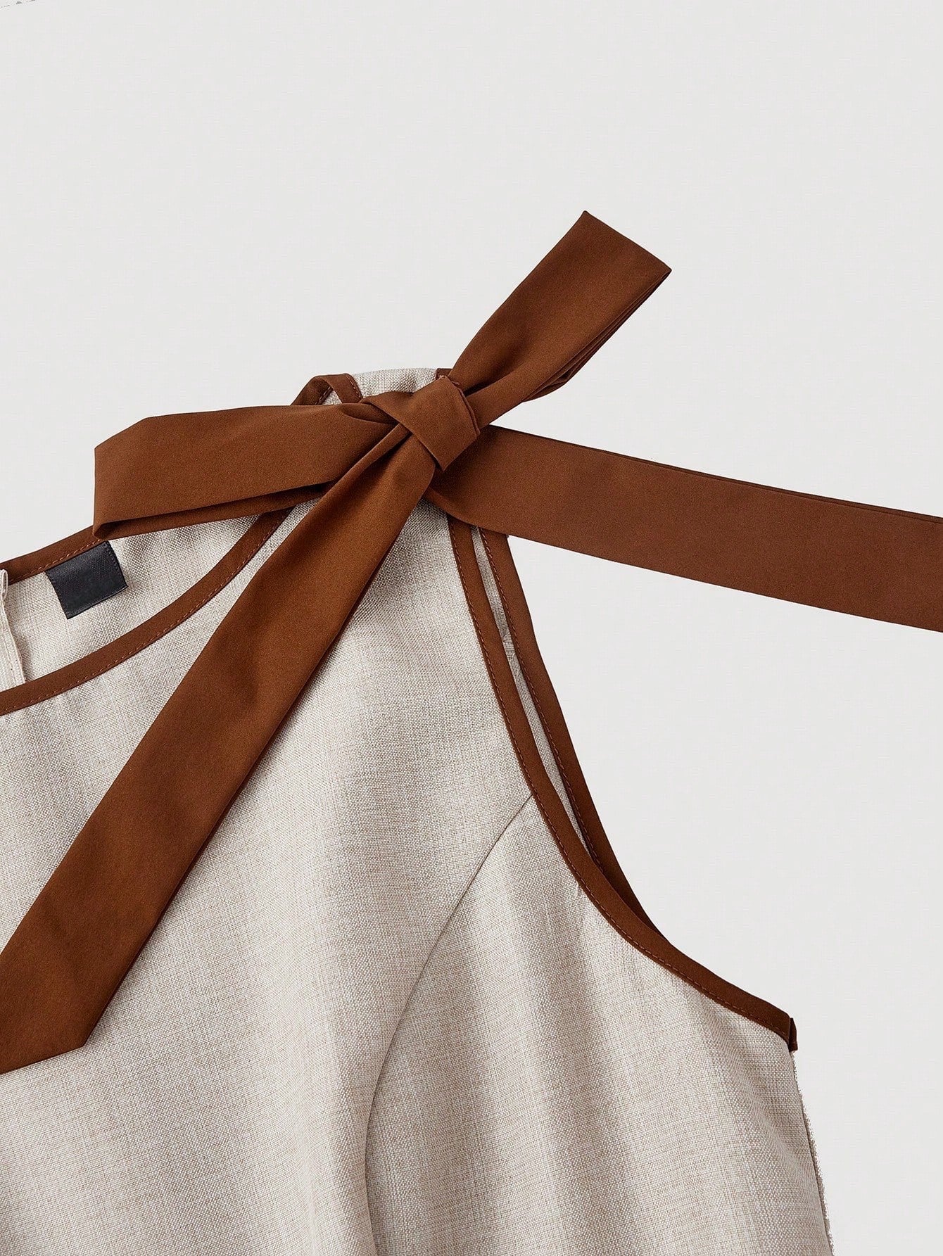 Khaki wide-leg sleeveless jumpsuit featuring contrast brown shoulder bow ties and trim laid flat against a neutral background