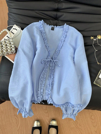 Light blue frill trim tie-front long-sleeve blouse with delicate ruffles laid flat on a dark textured background