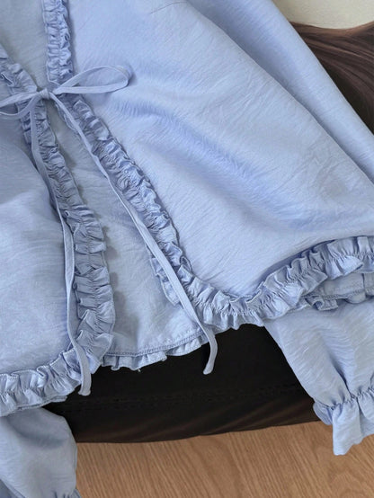 Light blue frill trim tie-front long-sleeve blouse with delicate ruffles laid flat on a dark textured background