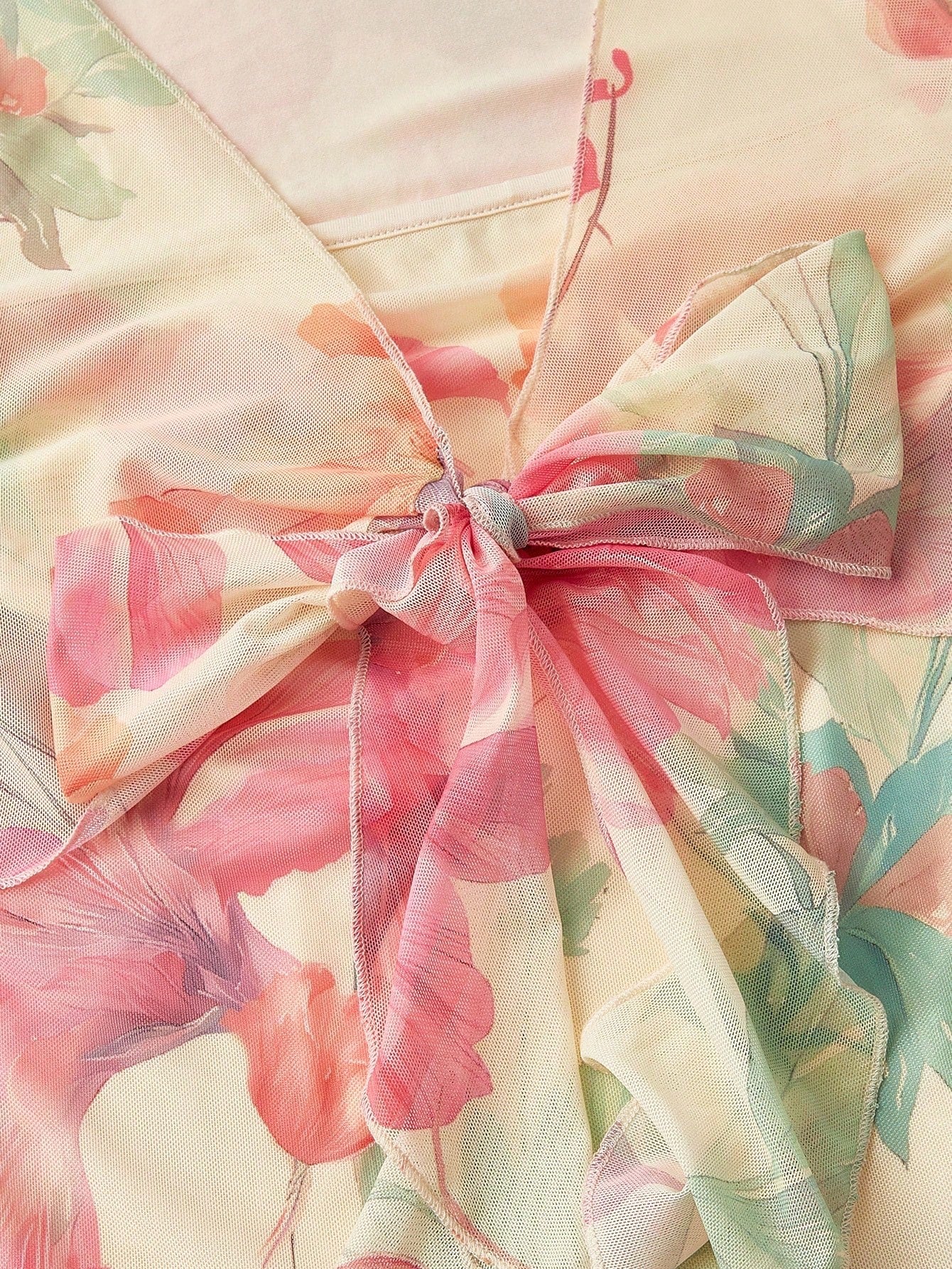 Pink and green floral print long-sleeve flare blouse with a V-neck and twist-front tie detail laid flat against a neutral background