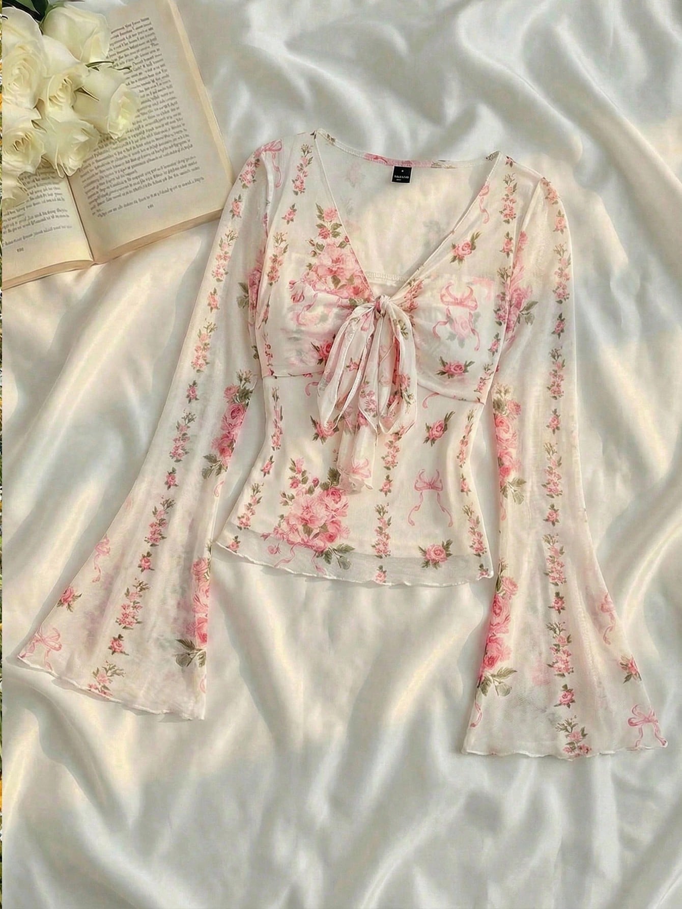 Pink and white floral print tie-front flare sleeve top laid flat against a neutral background