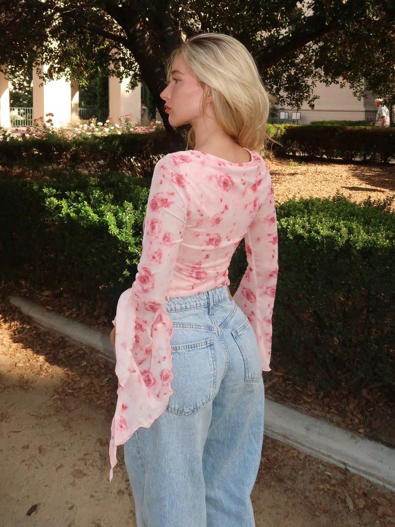 Pink floral print sheer mesh long-sleeve top with a tie-front closure, V-neck, and dramatic bell sleeves on a neutral background.