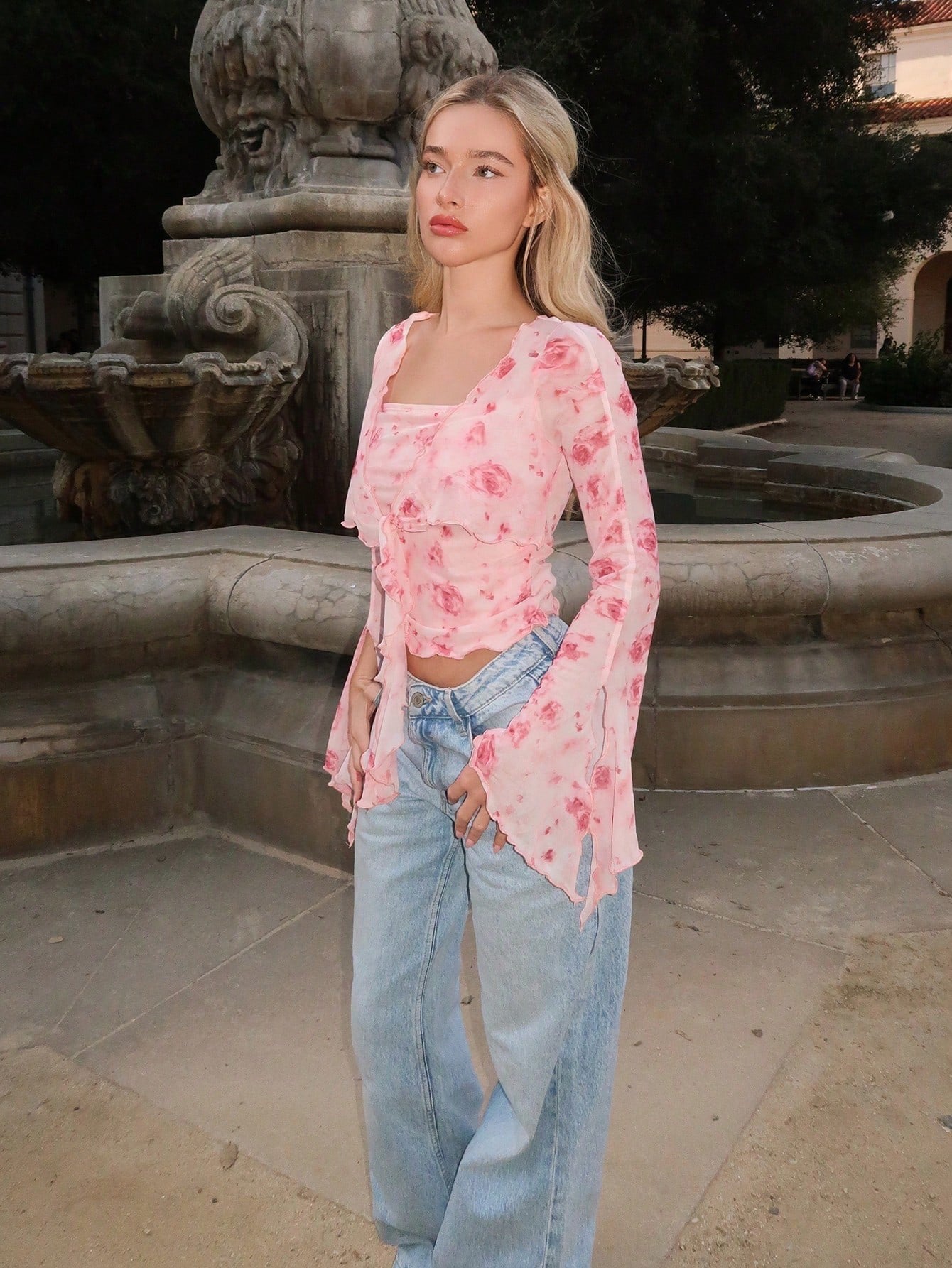 Pink floral print sheer mesh long-sleeve top with a tie-front closure, V-neck, and dramatic bell sleeves on a neutral background.
