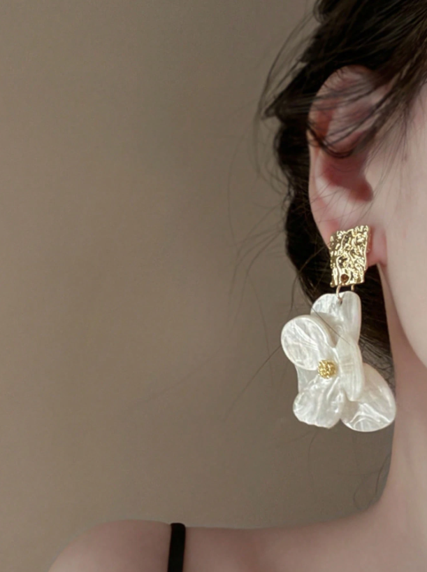 Close-up of a person wearing a floral earring with a beige background