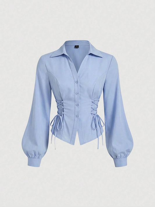 Solid color blue button-down shirt with lapel collar, lantern sleeves, and waist lace-up corset ties laid flat
