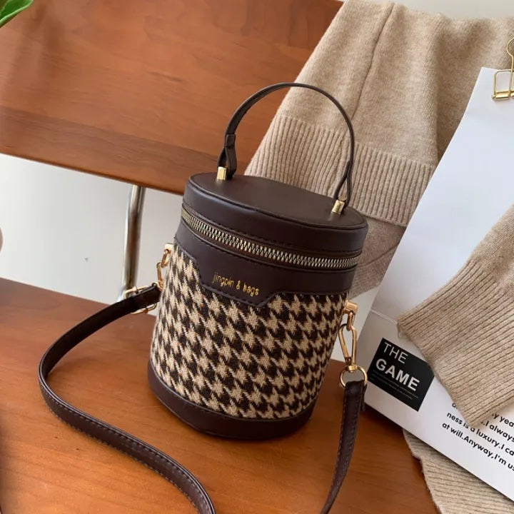 Houndstooth patterned handbag with brown leather accents on a wooden surface.