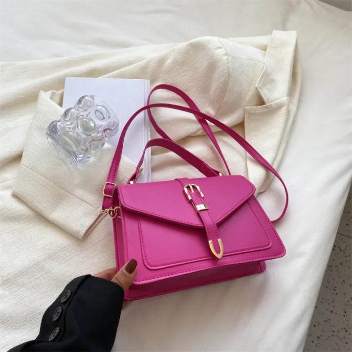 Pink handbag on a white surface with a hand holding it