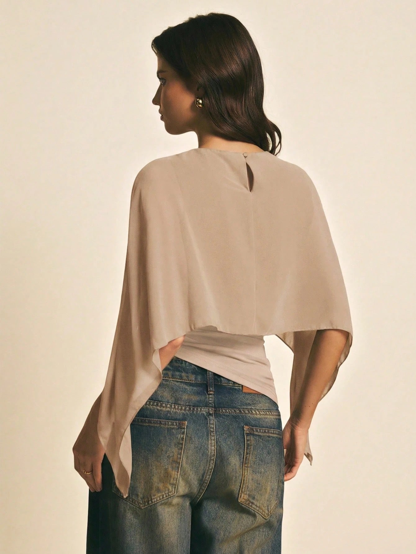 Woman wearing a Khaki solid color elegant shawl blouse with cape sleeves paired with dark denim jeans