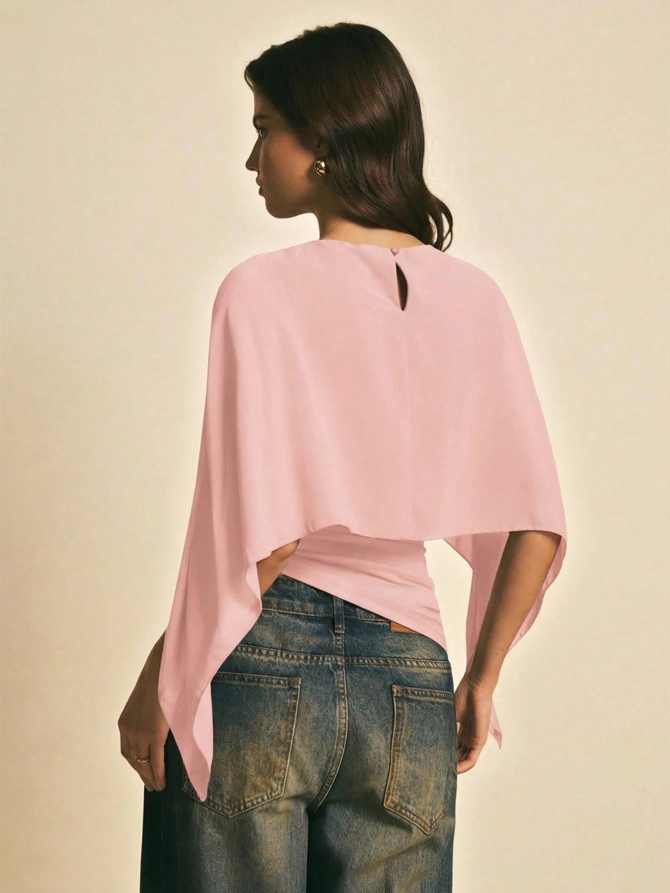 Woman wearing a Pink solid color elegant shawl blouse with cape sleeves paired with dark denim jeans