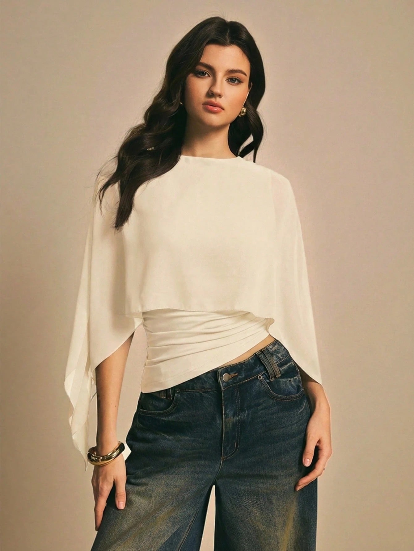 Woman wearing a apricot  solid color elegant shawl blouse with cape sleeves paired with dark denim jeans