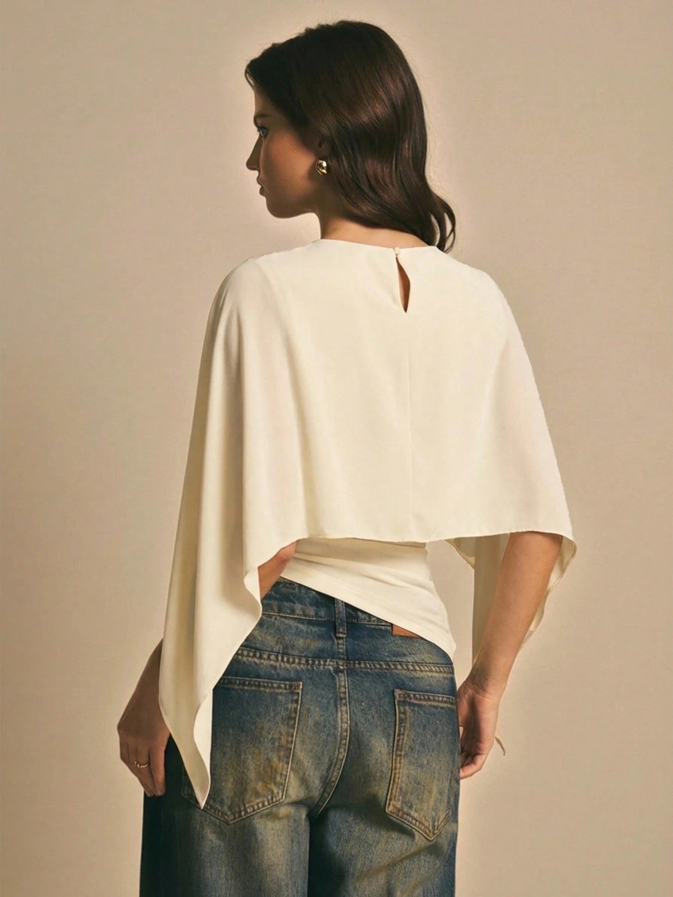 Woman wearing a apricot  solid color elegant shawl blouse with cape sleeves paired with dark denim jeans