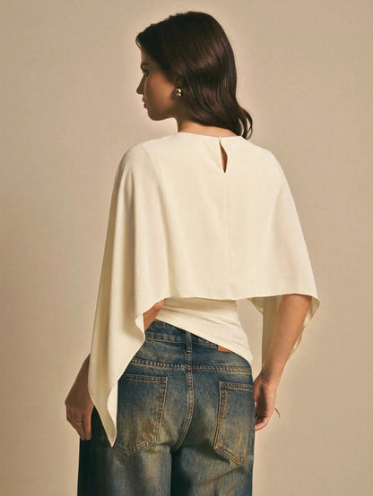 Woman wearing a apricot  solid color elegant shawl blouse with cape sleeves paired with dark denim jeans