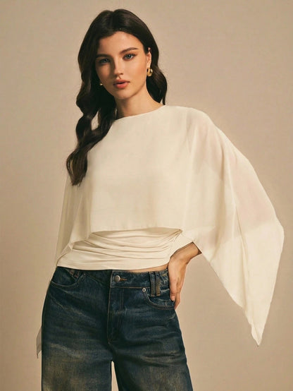 Woman wearing a apricot  solid color elegant shawl blouse with cape sleeves paired with dark denim jeans