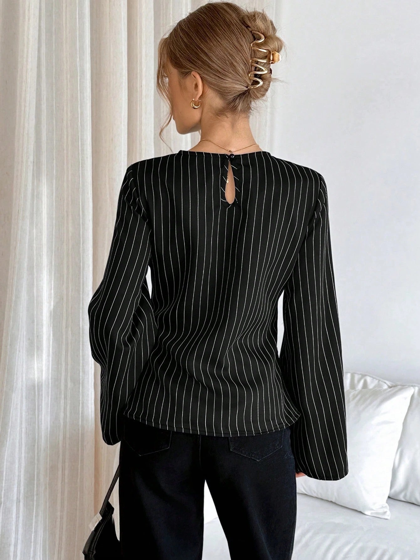 Woman wearing a black pinstripe long sleeve blouse featuring a metal ring decor waist detail and dark trousers
