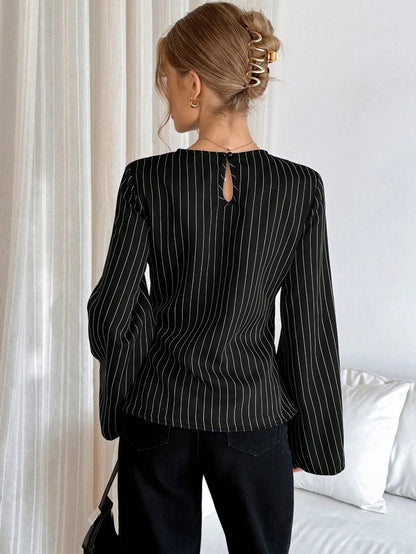 Woman wearing a black pinstripe long sleeve blouse featuring a metal ring decor waist detail and dark trousers