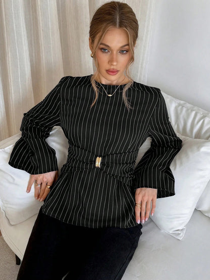 Woman wearing a black pinstripe long sleeve blouse featuring a metal ring decor waist detail and dark trousers