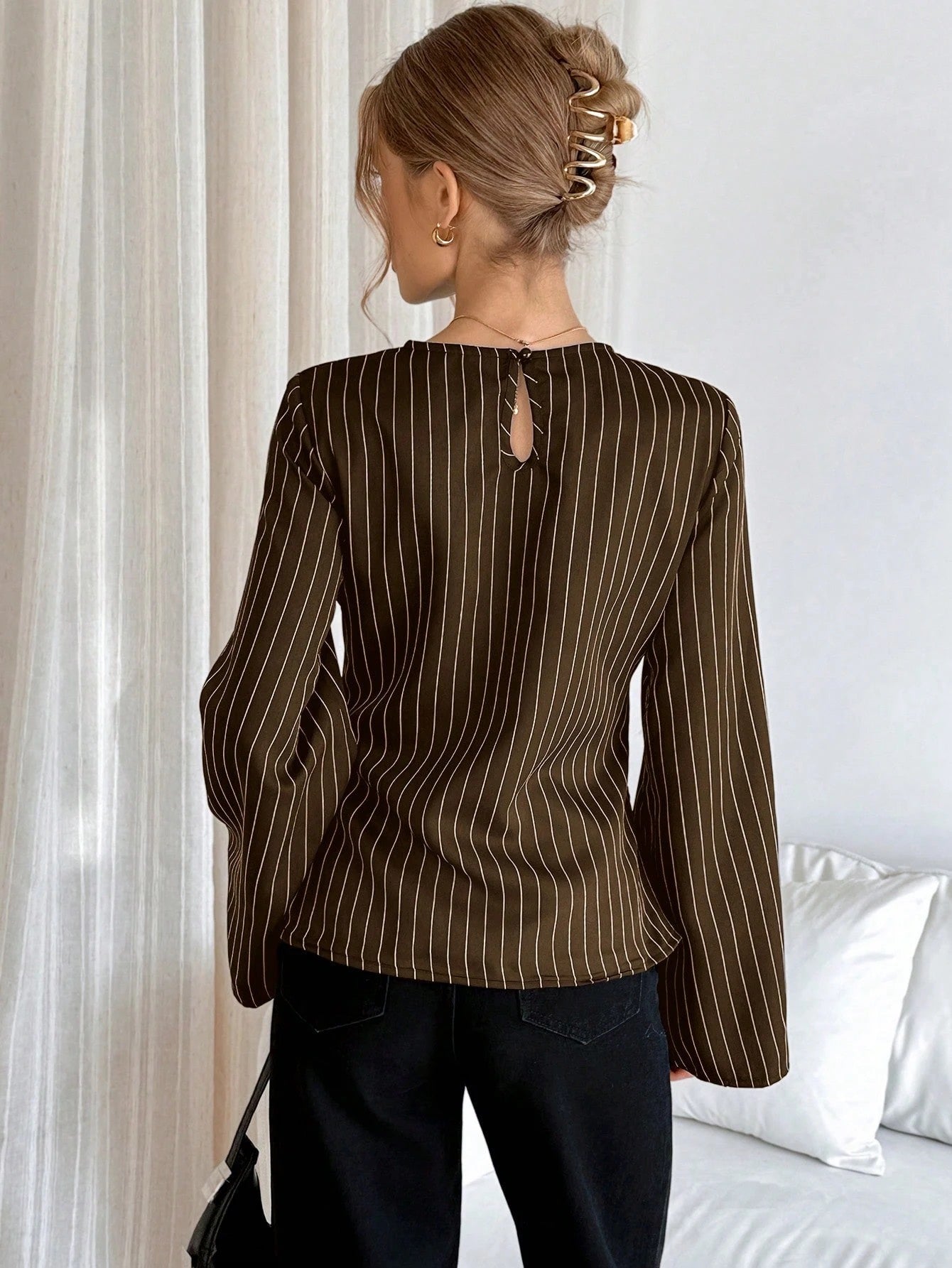 Woman wearing a brown pinstripe long sleeve blouse featuring a metal ring decor waist detail and dark trousers