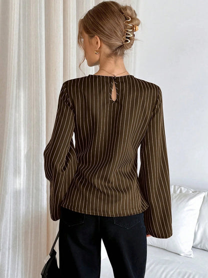 Woman wearing a brown pinstripe long sleeve blouse featuring a metal ring decor waist detail and dark trousers