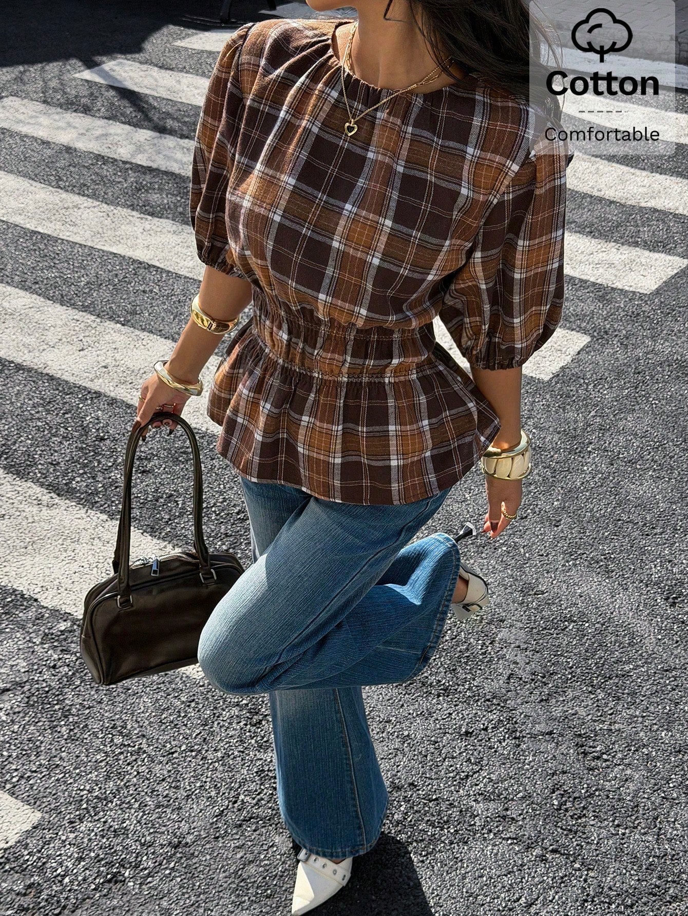 Woman wearing a brown plaid round neck short puff sleeve cinched waist blouse paired with blue jeans