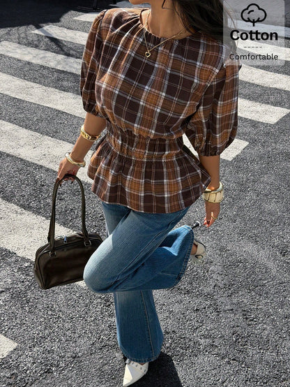 Woman wearing a brown plaid round neck short puff sleeve cinched waist blouse paired with blue jeans