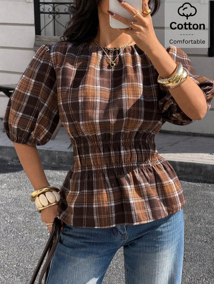 Woman wearing a brown plaid round neck short puff sleeve cinched waist blouse paired with blue jeans