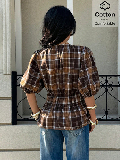 Woman wearing a brown plaid round neck short puff sleeve cinched waist blouse paired with blue jeans