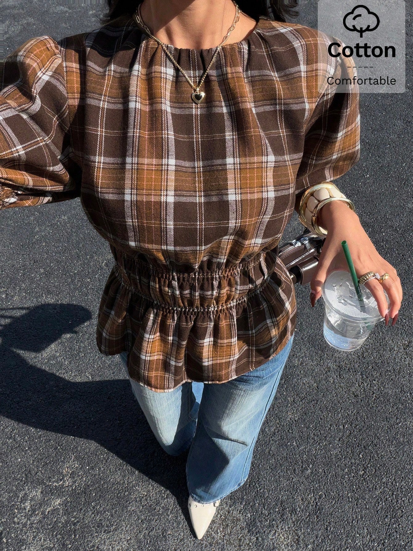 Woman wearing a brown plaid round neck short puff sleeve cinched waist blouse paired with blue jeans