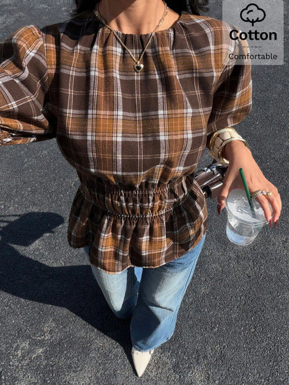 Woman wearing a brown plaid round neck short puff sleeve cinched waist blouse paired with blue jeans