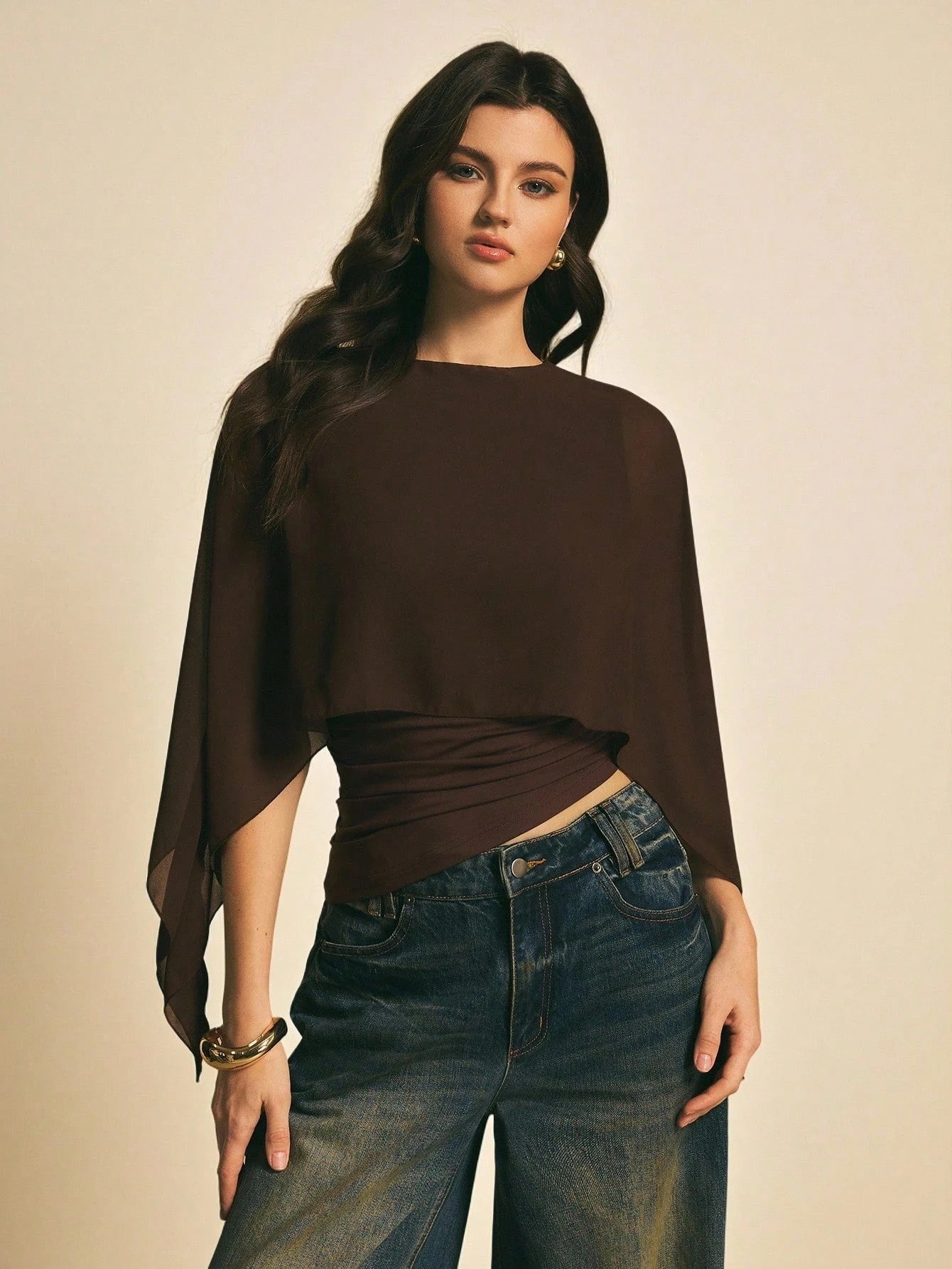 Woman wearing a brown solid color elegant shawl blouse with cape sleeves paired with dark denim jeans
