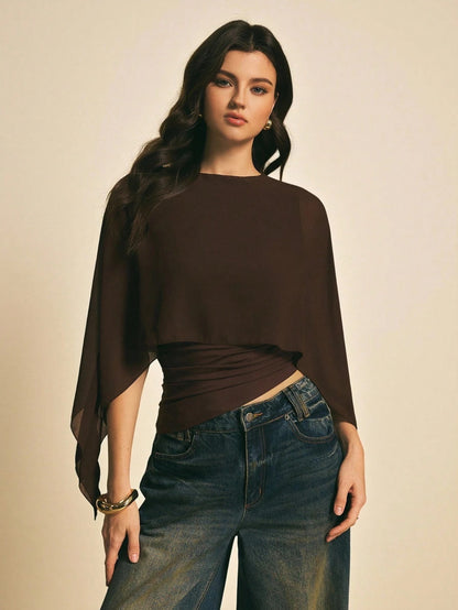 Woman wearing a brown solid color elegant shawl blouse with cape sleeves paired with dark denim jeans