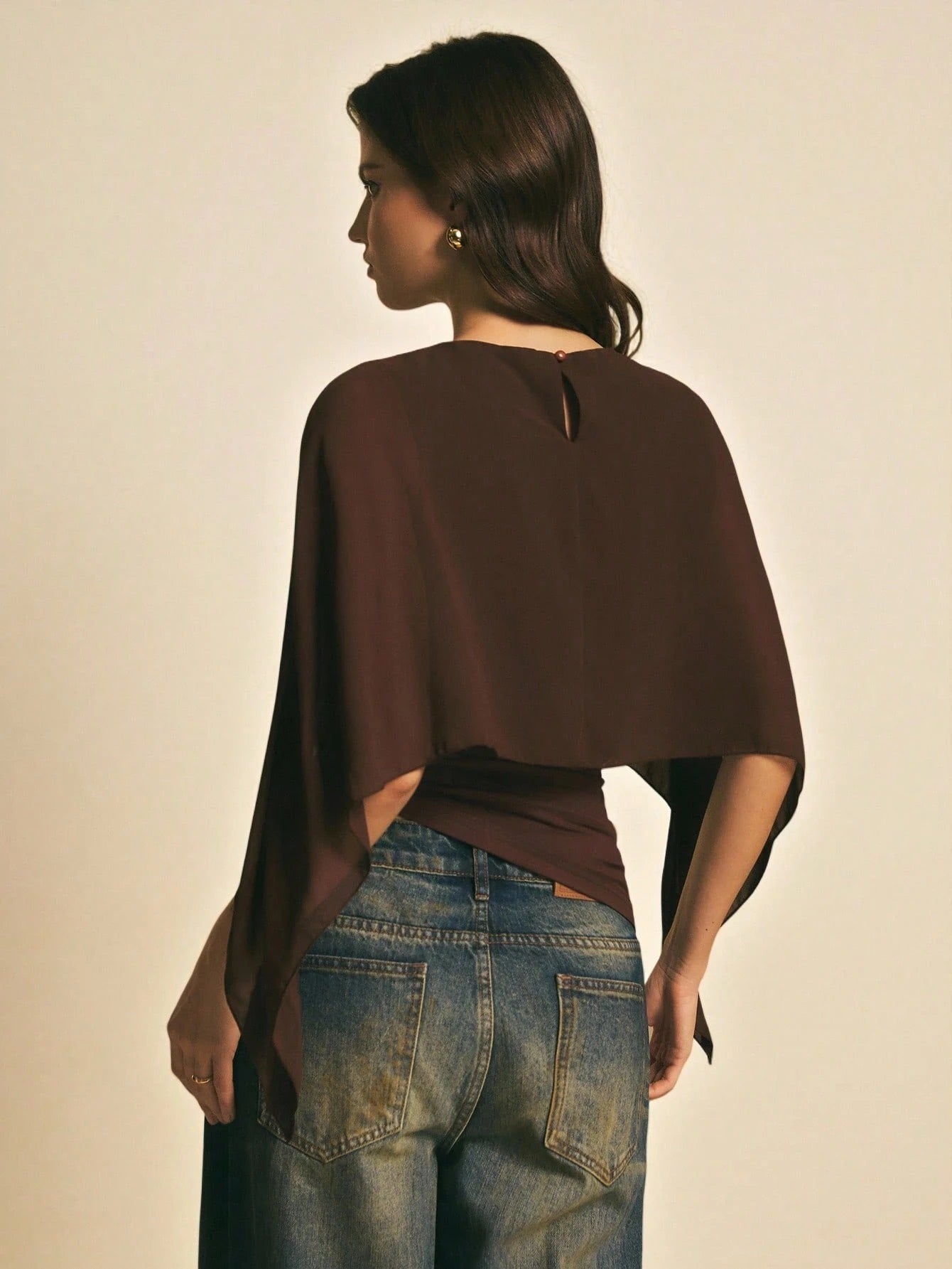 Woman wearing a brown solid color elegant shawl blouse with cape sleeves paired with dark denim jeans