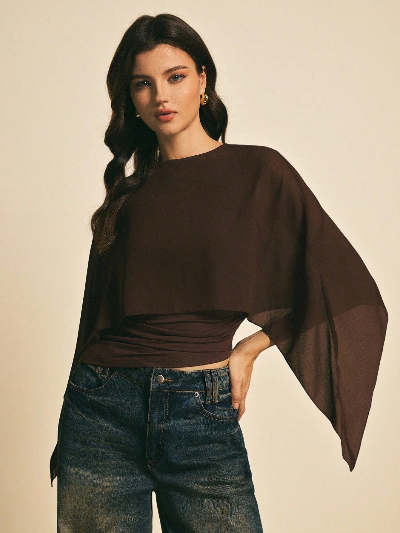 Woman wearing a brown solid color elegant shawl blouse with cape sleeves paired with dark denim jeans