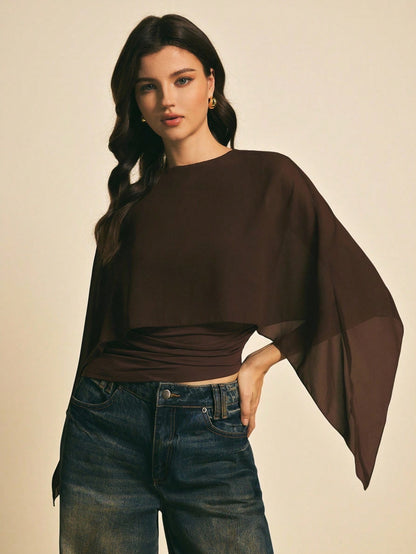 Woman wearing a brown solid color elegant shawl blouse with cape sleeves paired with dark denim jeans