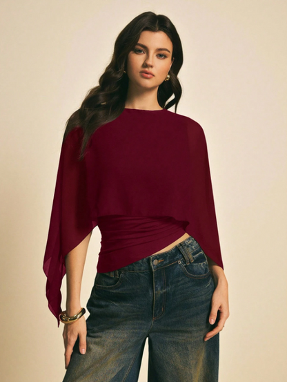 Woman wearing a burgundy solid color elegant shawl blouse with cape sleeves paired with dark denim jeans