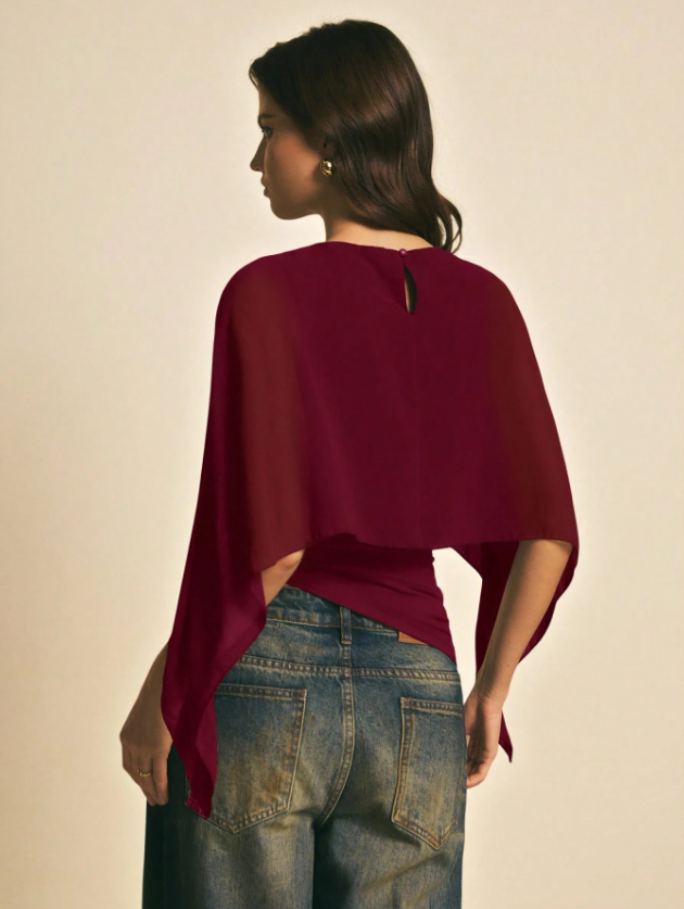 Woman wearing a burgundy solid color elegant shawl blouse with cape sleeves paired with dark denim jeans