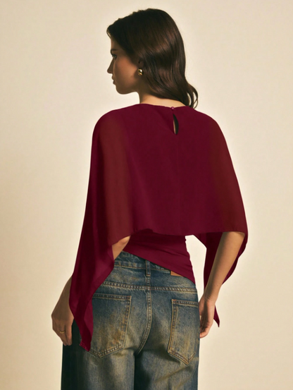 Woman wearing a burgundy solid color elegant shawl blouse with cape sleeves paired with dark denim jeans