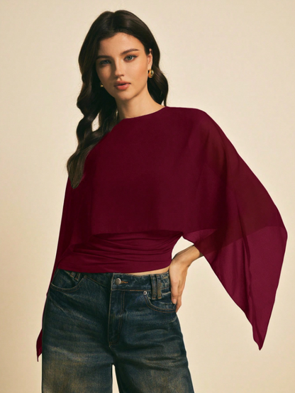 Woman wearing a burgundy solid color elegant shawl blouse with cape sleeves paired with dark denim jeans