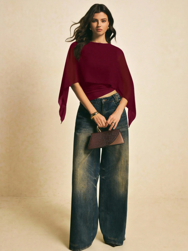 Woman wearing a burgundy solid color elegant shawl blouse with cape sleeves paired with dark denim jeans