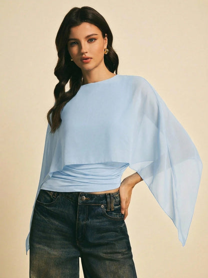 Woman wearing a light blue solid color elegant shawl blouse with cape sleeves paired with dark denim jeans